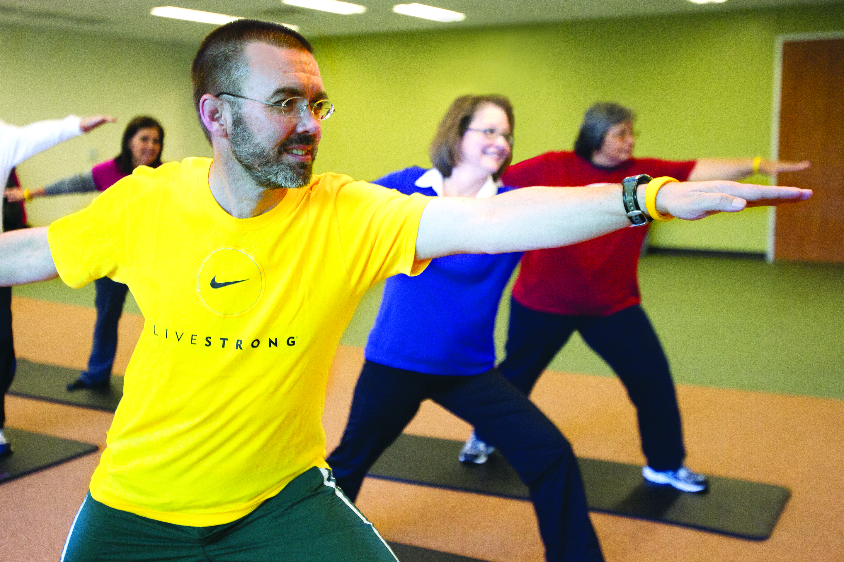 A group of adults doing yoga, one in a bright yellow LIVESTRONG shirt