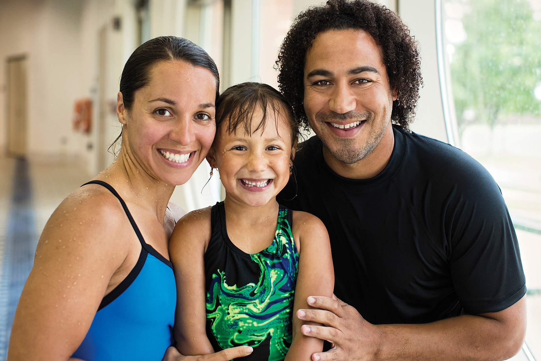 A mother and father smiling with their daughter next to an indoor pool