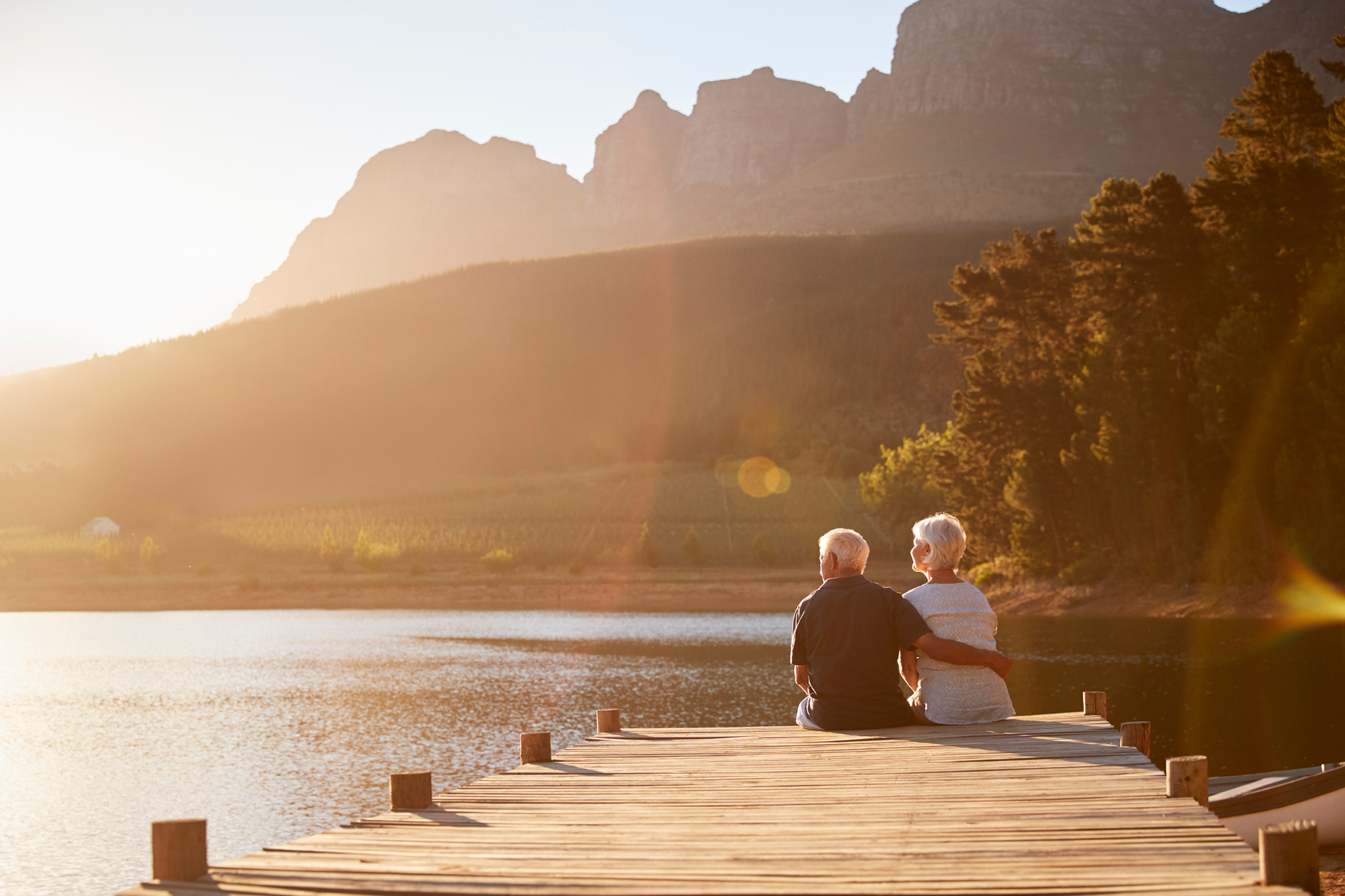 An older couple sitting at the end of a dock watching the sun set over a lake