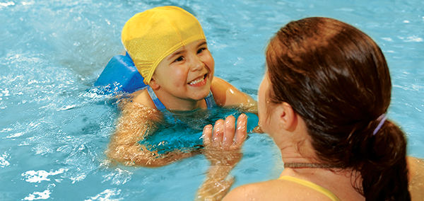 Swim Lessons with instructor and child. Photo inside of the pool child has on yellow swim cap.