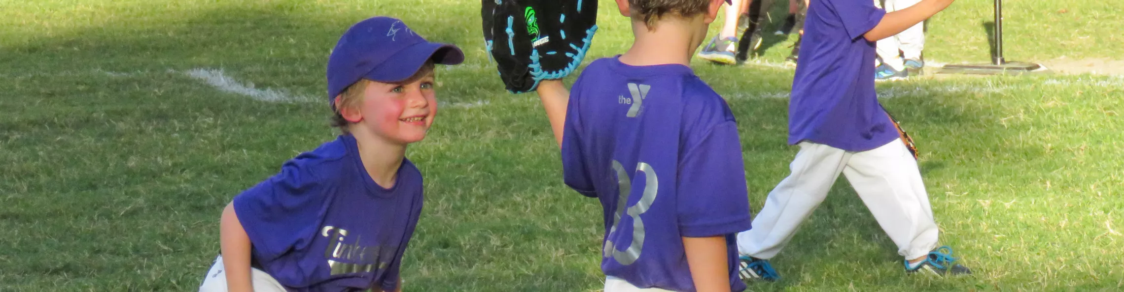 Youth Baseball participant smiling in a purple jersey and baseball cap 