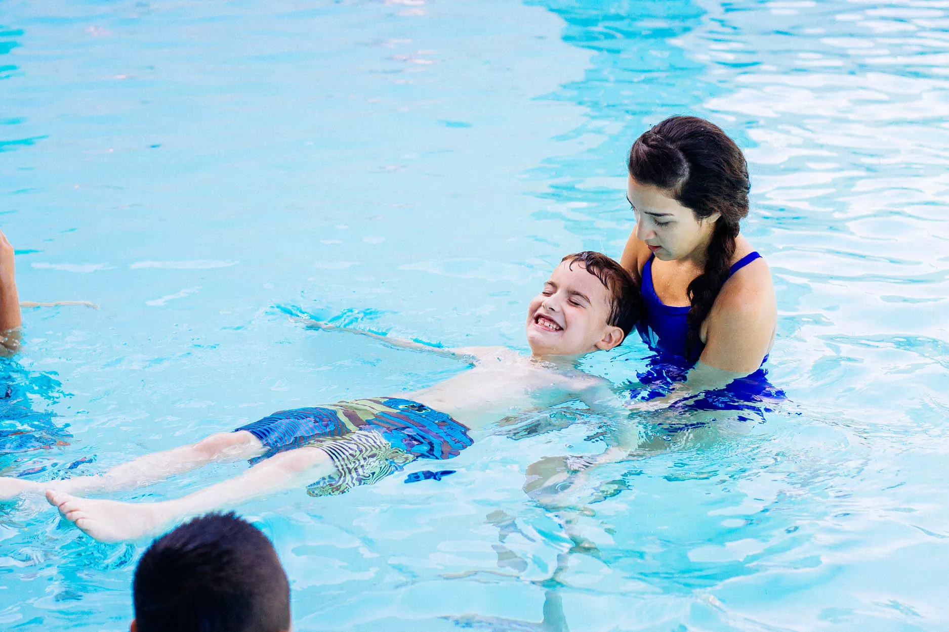 Lifeguard assisting male child with back floating during swim lesson