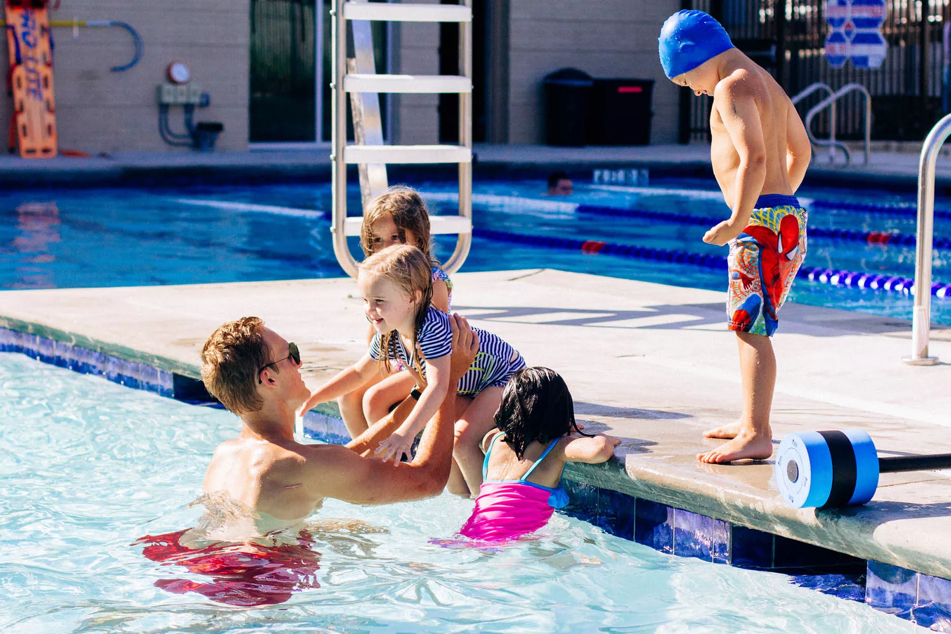 Lifeguard lifting female child into the pool while other children look on