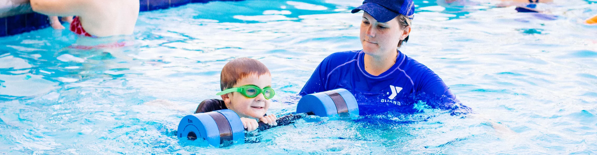 Lifeguard assisting male child during a swim lesson using a flotation device