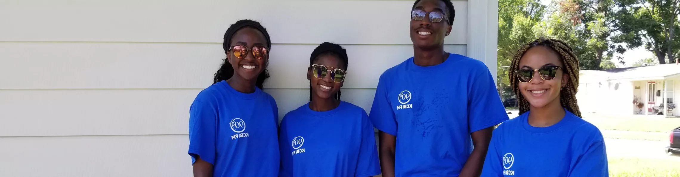 Four teens in blue shirts smiling during a community service day